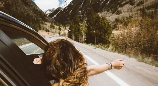 woman riding on vehicle putting her head and right arm outside the window while travelling the road